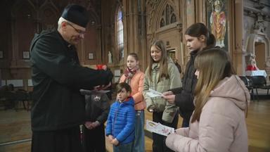 Ein Geistlicher übergibt einer Gruppe von fünf Kindern etwas in einer Kirche.