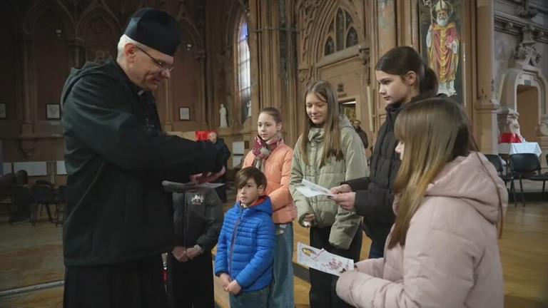 Ein Geistlicher übergibt einer Gruppe von fünf Kindern etwas in einer Kirche.