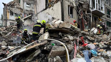 Zerstörtes Haus, viel Schutt. Darauf einige Feuerwehrleute in ihren Anzügen.