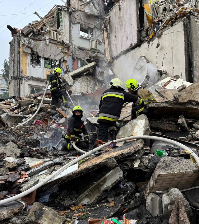Zerstörtes Haus, viel Schutt. Darauf einige Feuerwehrleute in ihren Anzügen.