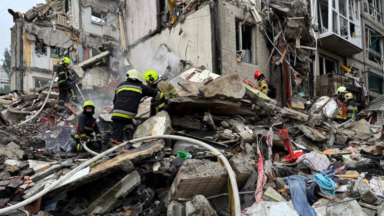 Zerstörtes Haus, viel Schutt. Darauf einige Feuerwehrleute in ihren Anzügen.