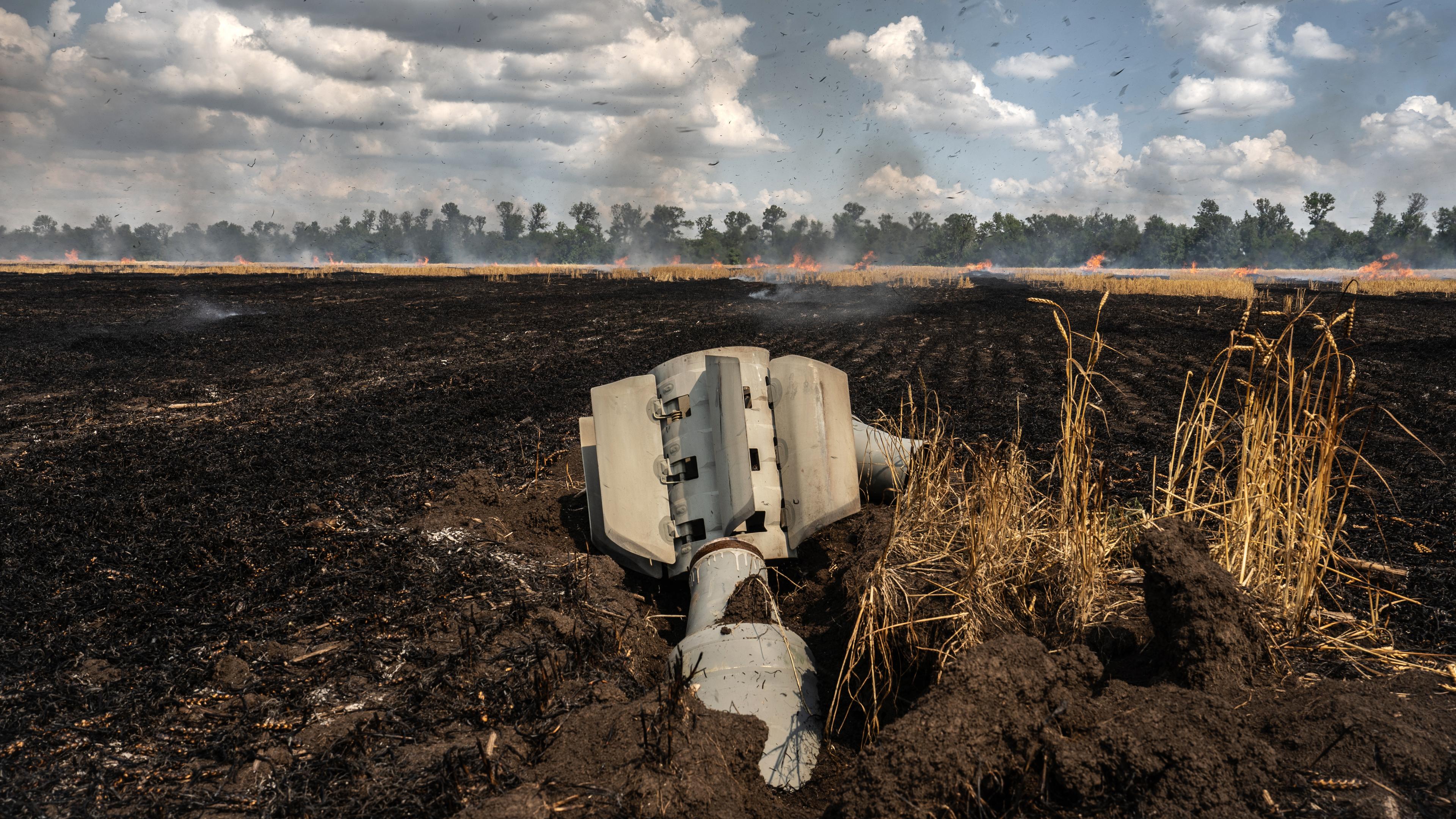 Eine Rakete liegt auf einem Weizenfeld, im Hintergrund ist ein Feuer zu sehen.