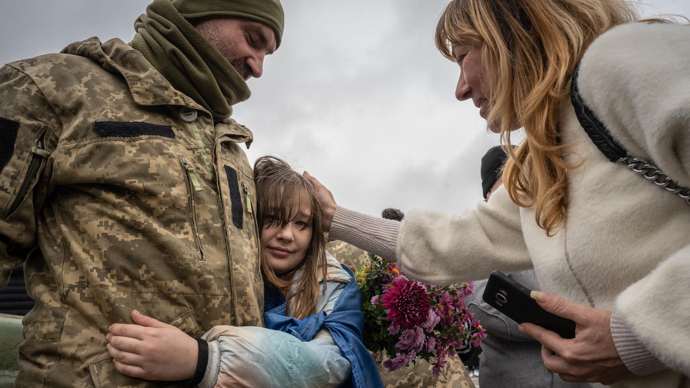 Ein Mädchen umarmt einen Soldaten und wird von einer Frau am Kopf gestreichelt.