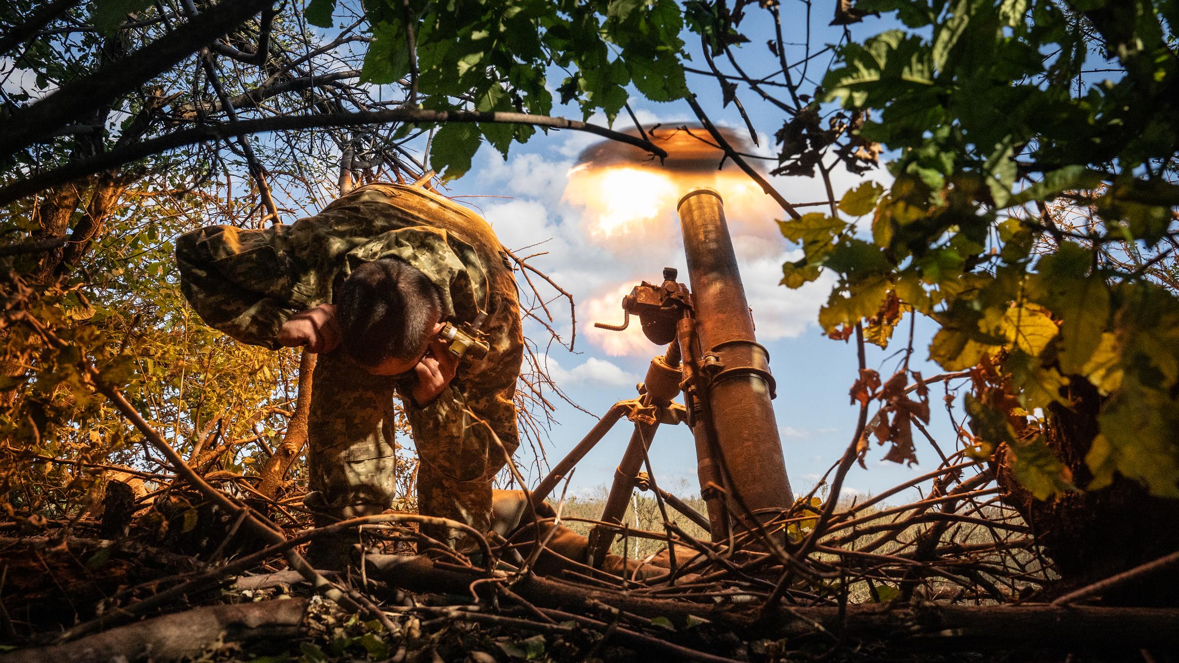 Ein Soldat hält sich die Ohren zu, während sich neben ihm ein Schuss löst.
