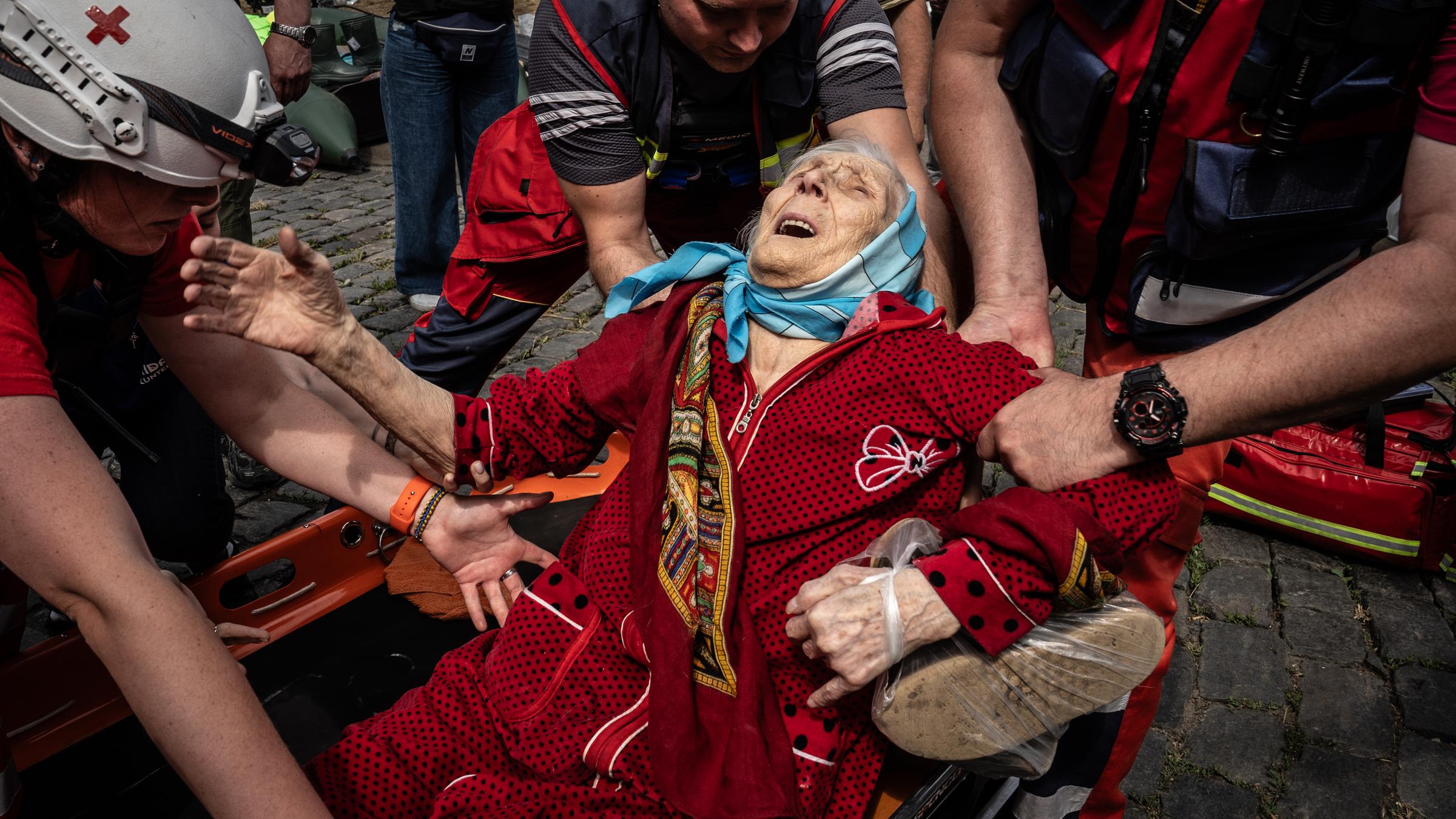 Eine ältere Frau wird aus ihrem Haus getragen.