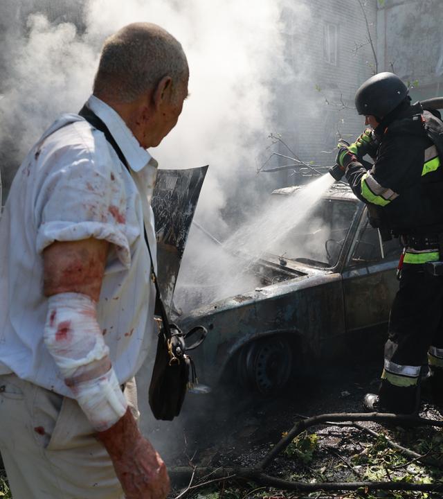 Ein Feuerwehrmann löscht in Anwesenheit eines verletzten Anwohners ein brennendes Auto in Saporischschja.