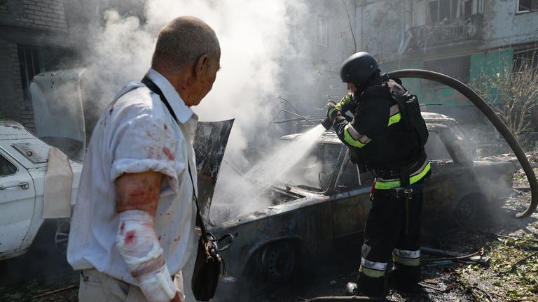 Ein Feuerwehrmann löscht in Anwesenheit eines verletzten Anwohners ein brennendes Auto in Saporischschja.