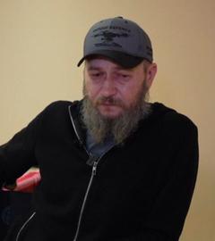 Soldat Vlasenko. Ein älter aussehender Mann mit langem grauen Bart und einer dunkelblauen Cap auf, auf der eine Drohne sichtbar ist.