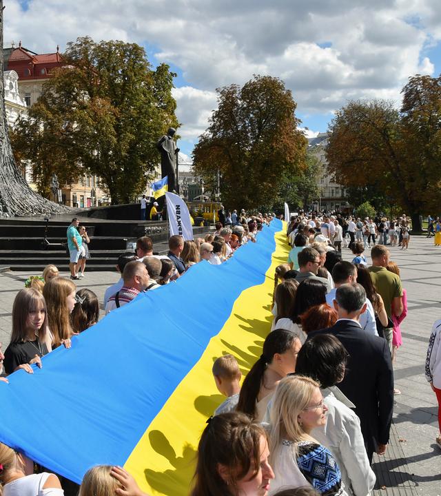 Ukrainer gehen mit der Nationalflagge durch die Stadt.