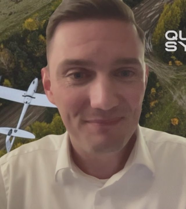 Quantum-Systems Sprecher Paul Strobel vor Grafik einer Landschaft mit Drohne.