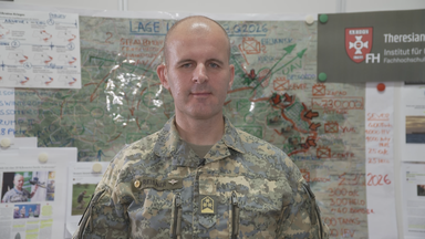 Oberst Markus Reisner in Militär-Camoflage-Uniform mit einer Militärkarte im Hintergrund.