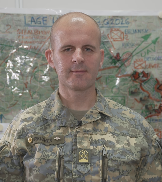 Oberst Markus Reisner in Militär-Camoflage-Uniform mit einer Militärkarte im Hintergrund.
