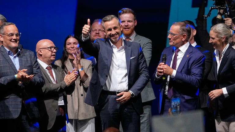 Ulrich Siegmund von der AfD streckt seinen Daumen nach dem Wahlsieg hoch aus und lächelt. Er ist umgeben von anderen AfD-Parteimitgliedern sowie Alice Weidel und Tino Chrupalla.