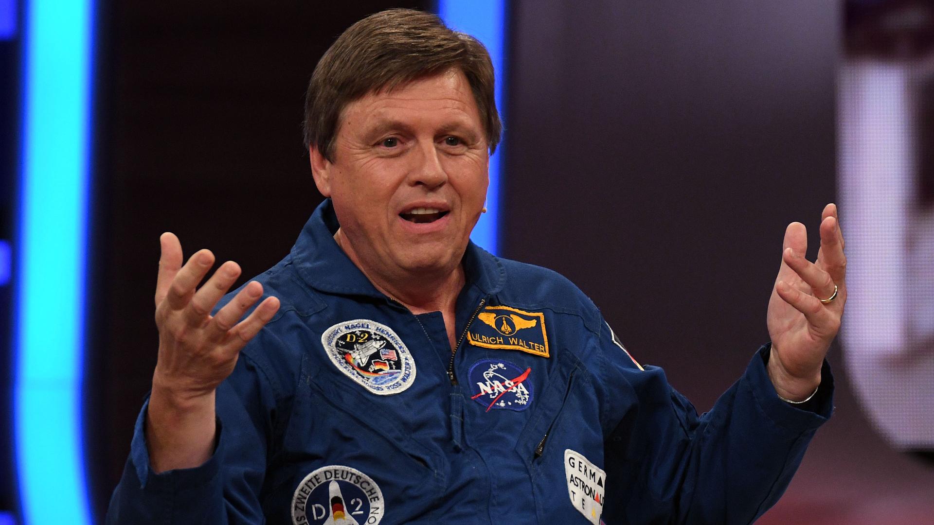 Der Astronaut Ulrich Waltersitzt auf einer Couch, gestikuliert und spricht.