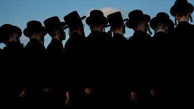 Ultraorthodoxe jüdische Männer beten auf einem Hügel mit Blick auf das Mittelmeer, während sie an einer Zeremonie teilnehmen. 
