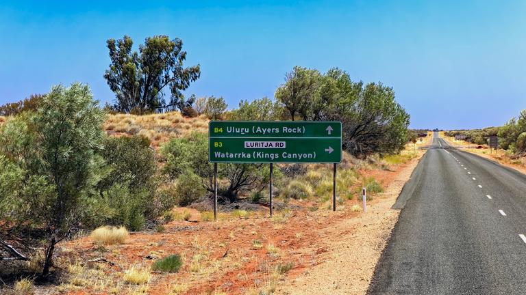 Ein Schild auf dem Lasseter Highway im australischen Outback zeigt die Richtung "Uluru/Ayers Rock".