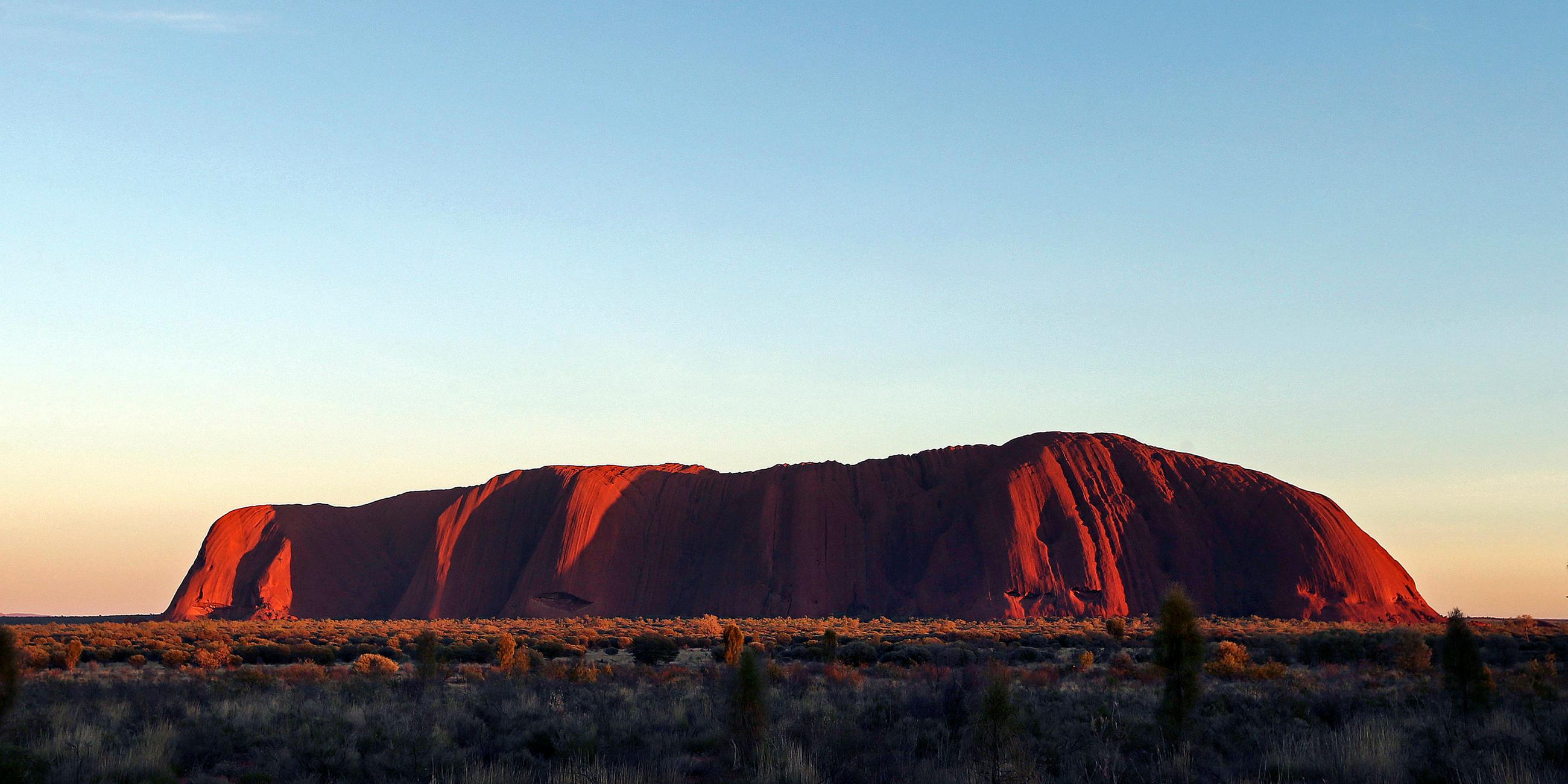 Der Uluru in Australien leuchtet in rot während des Sonnenaufgangs
