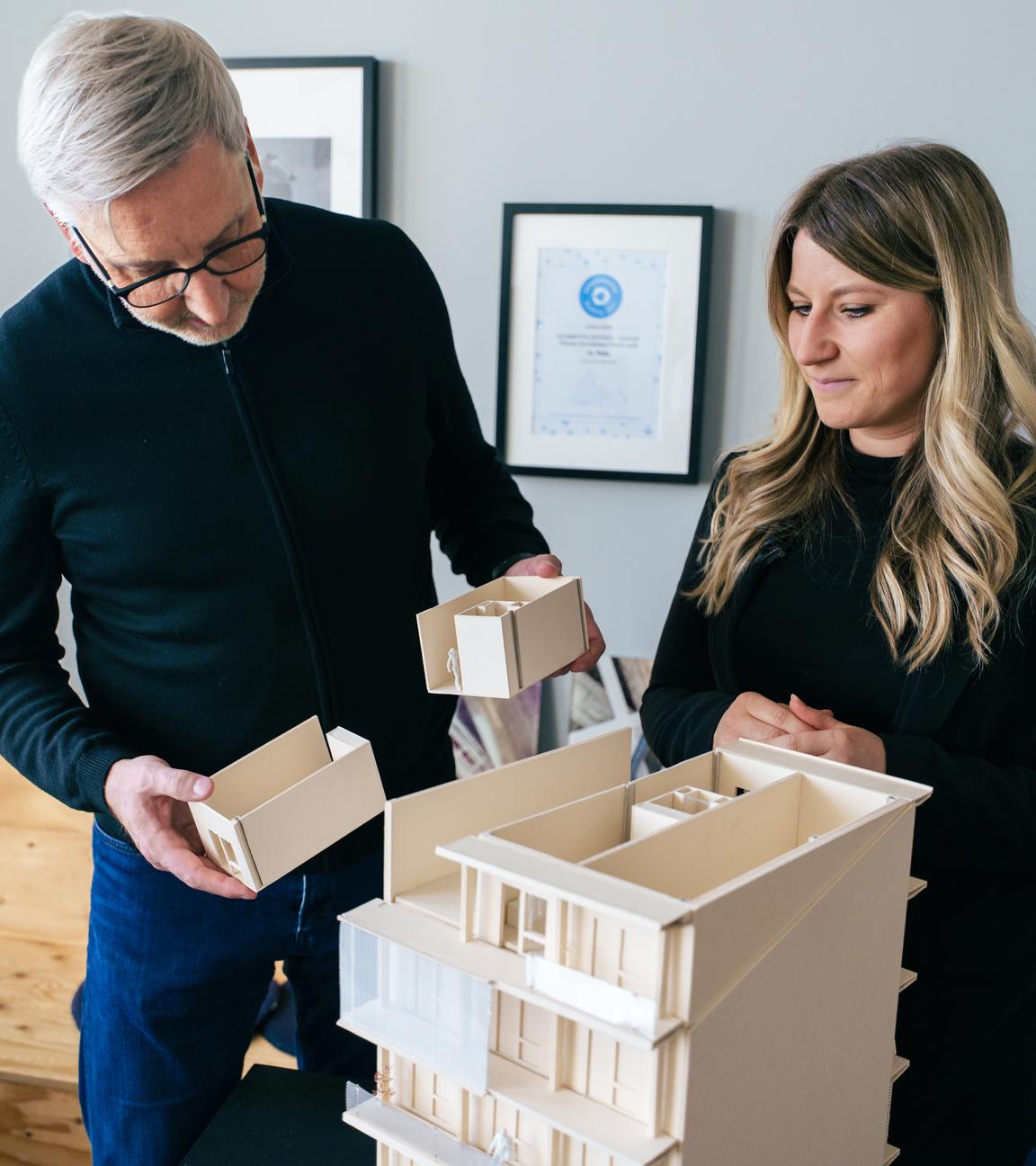 Architekt Markus Plöcker zeigt einer Frau das Arbeitsmodell von einem Gebäude aus Holz.