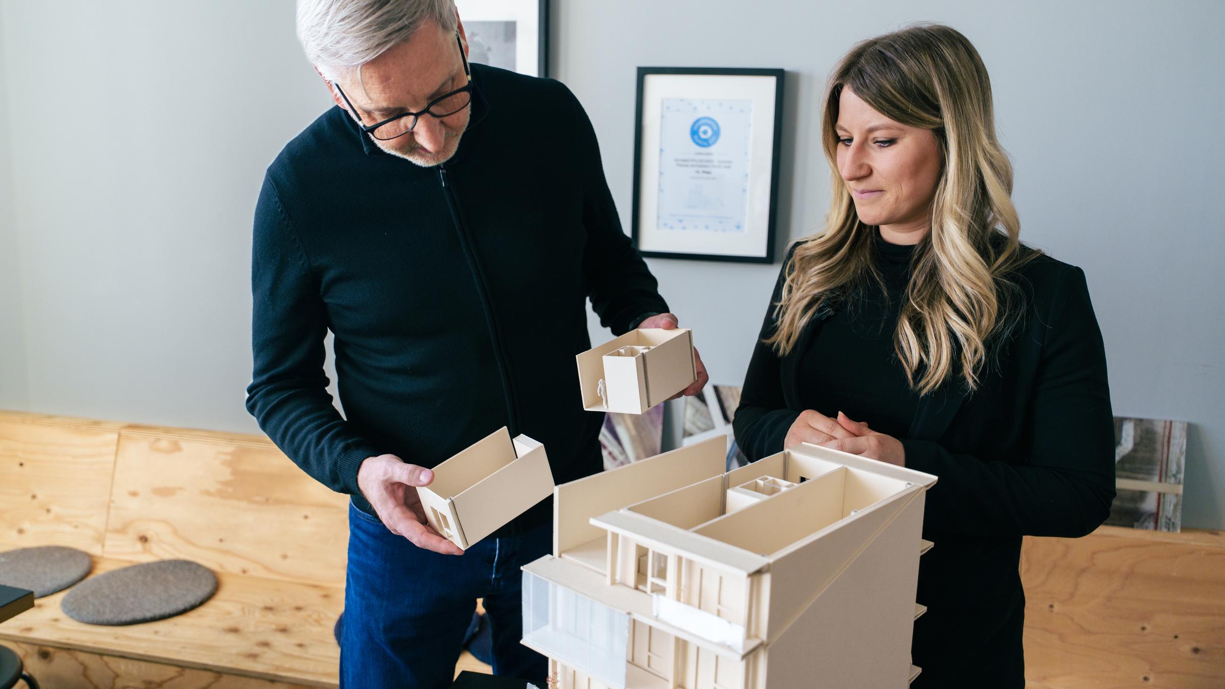 Architekt Markus Plöcker zeigt einer Frau das Arbeitsmodell von einem Gebäude aus Holz.
