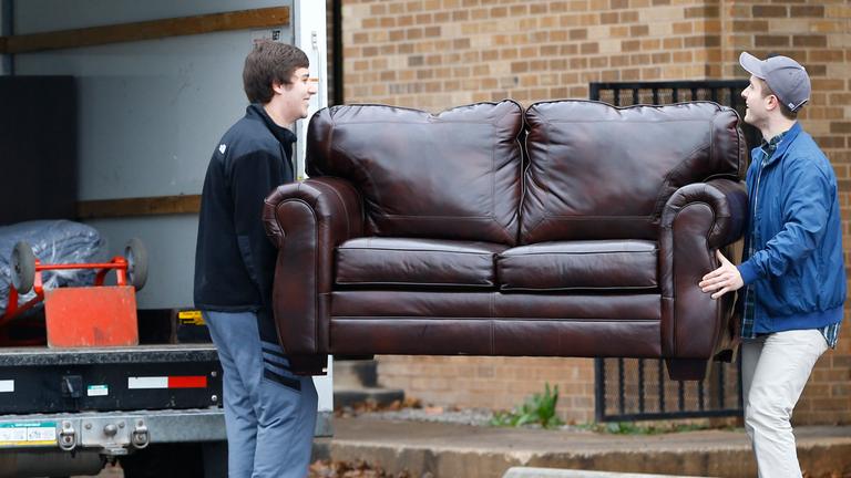 Zwei junge Männer tragen ein Sofa in einen Transporter.