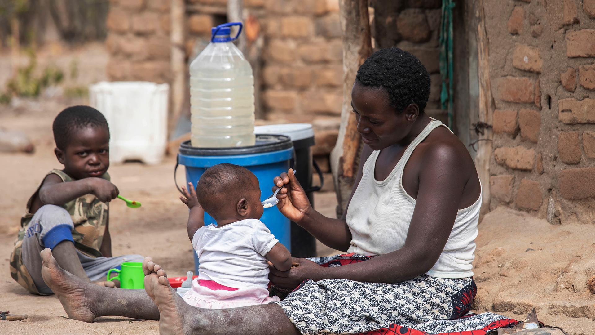 Mutter füttert Kinder auf dem Boden sitzend
