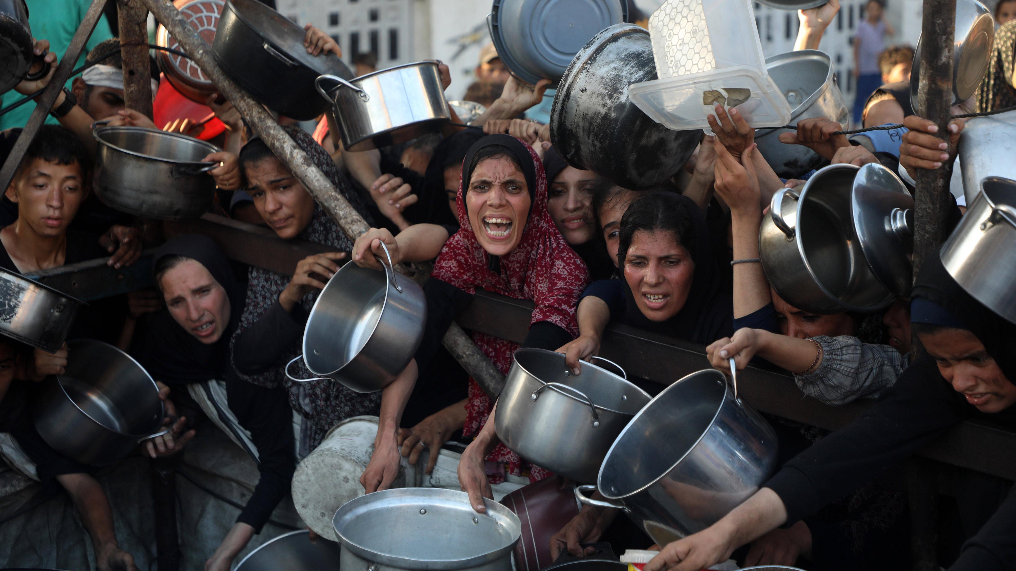Palästinenser warten mit Töpfen und anderen Gefäßen an einer Essensausgabe in Gaza-Stadt.