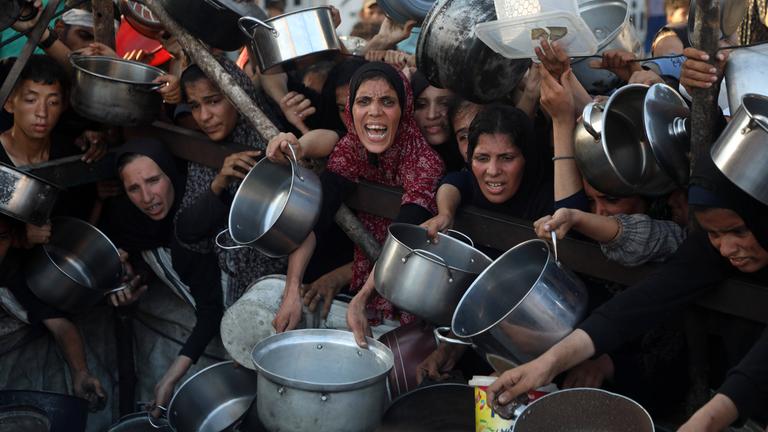 Palästinenser warten mit Töpfen und anderen Gefäßen an einer Essensausgabe in Gaza-Stadt.