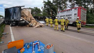 Das Bild zeigt eine Unfallstelle. Es sind mehrere große Fahrzeuge, teilweise beschädigt, zu sehen. Rechts im Bild sind mehrere Einsatzkräfte