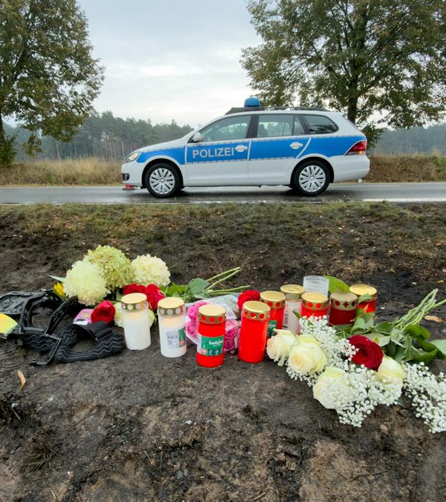 Unfallstelle mit Kerzen und Blumen, im Hintergrund ein Polizeiauto