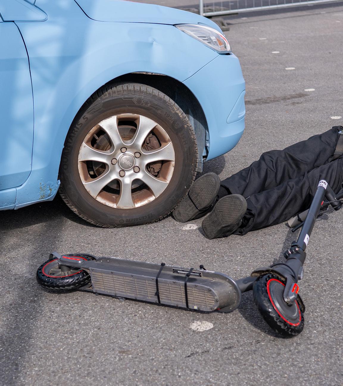  Bei einem Crashtest liegt ein E-Scooter Fahrer neben einem PKW, der ihn beim Crash seitlich erfasst hatte. Forscher stellen Studie zu Unfällen mit E-Scootern vor.