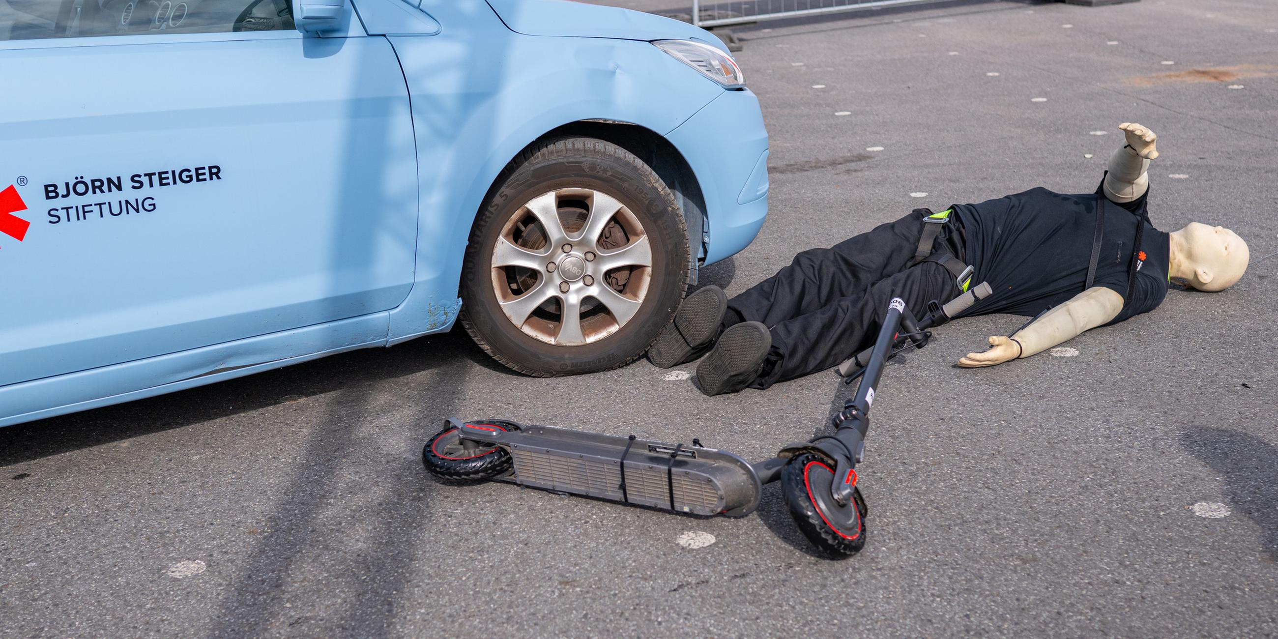 Bei einem Crashtest liegt ein E-Scooter Fahrer neben einem PKW, der ihn beim Crash seitlich erfasst hatte. Forscher stellen Studie zu Unfällen mit E-Scootern vor.