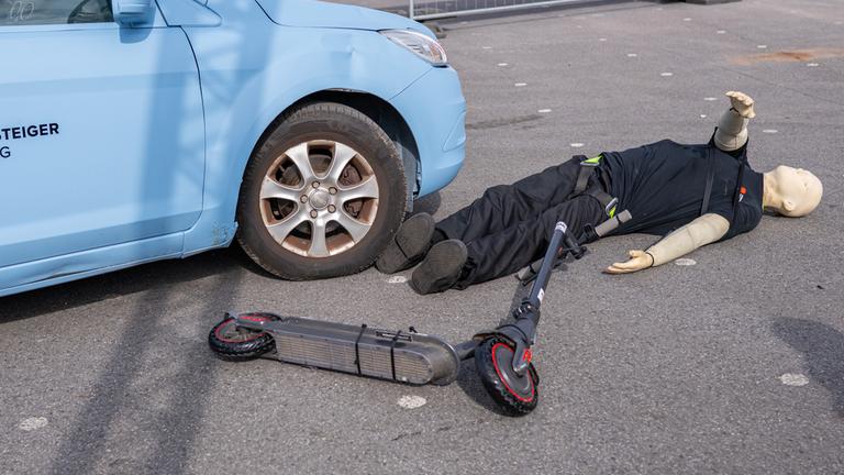  Bei einem Crashtest liegt ein E-Scooter Fahrer neben einem PKW, der ihn beim Crash seitlich erfasst hatte. Forscher stellen Studie zu Unfällen mit E-Scootern vor.