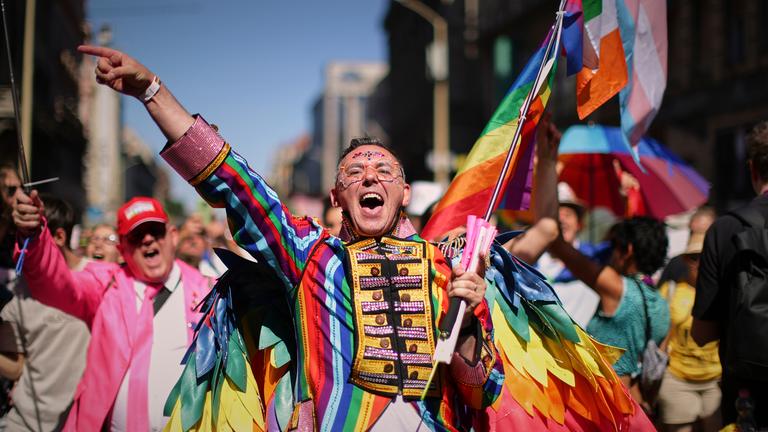 Ein bunt kostümierter Teilnehmer des Pride-Marsches in Budapest jubelt. 