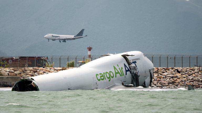 Ein Flugzeug, das neben einem Frachtflugzeug landet, liegt teilweise im Meer, nachdem es bei der Landung auf dem Hongkong International Airport am 19.10.2025 in Hongkong von der Landebahn abgekommen ist. 