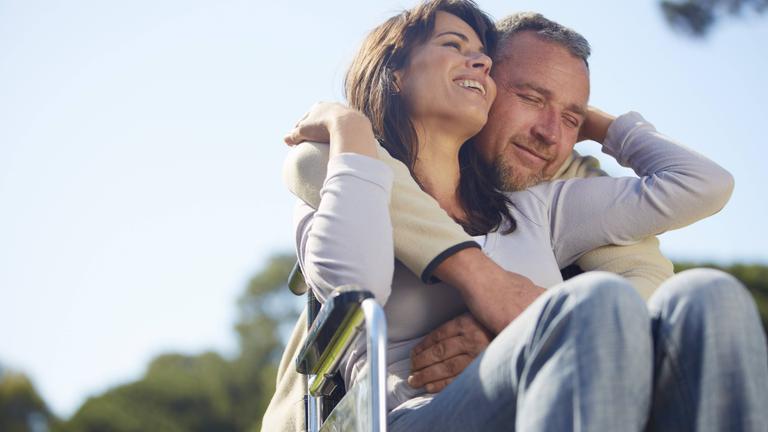 Ehepaar, er im Rollstuhl, sie schenkt ihm Blumen