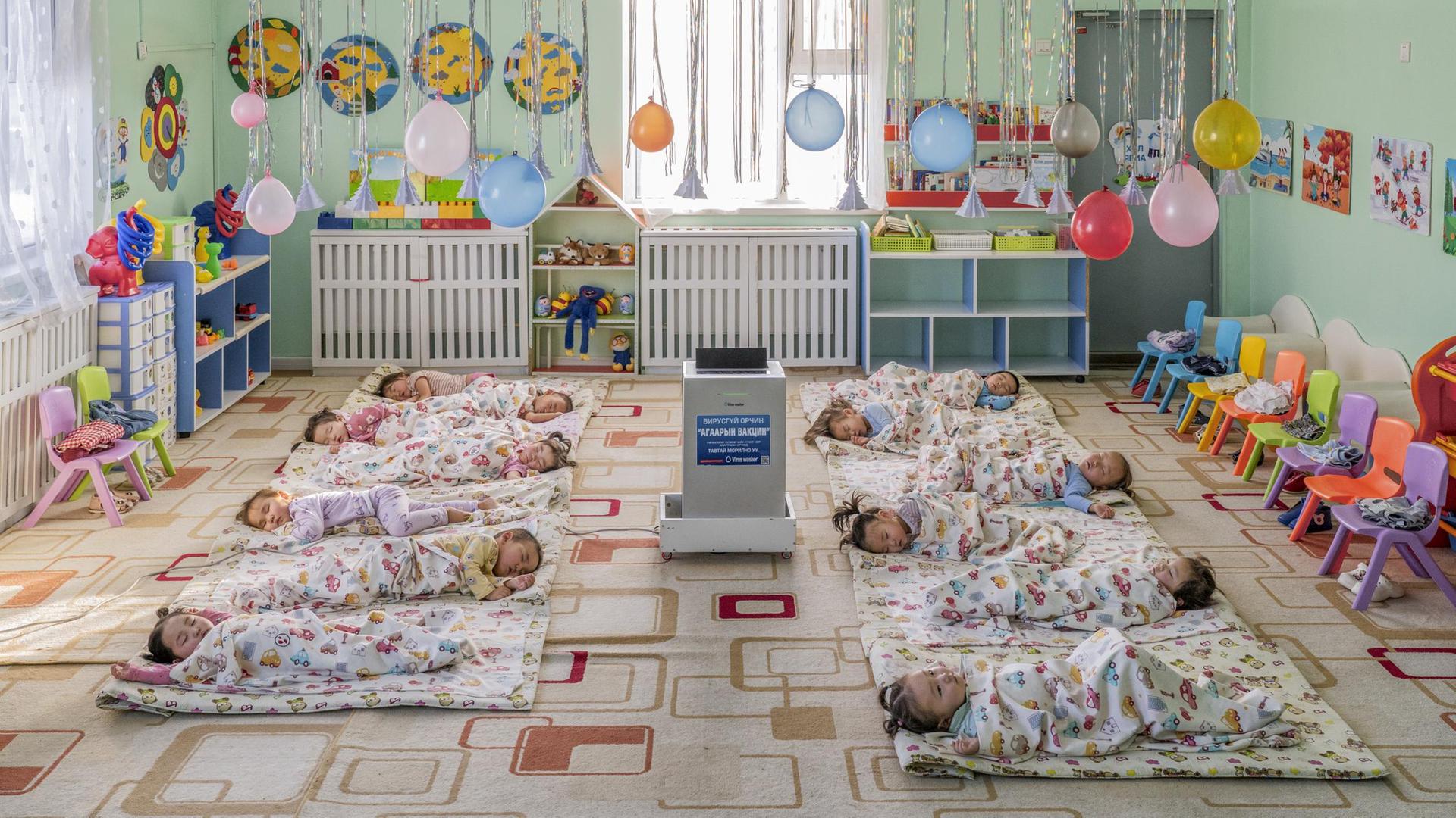 In einem Kindergarten in Ulaanbaatar, der Hauptstadt der Mongolei, liegen Kinder auf dem Boden um einen aufgestellten Luftfilter herum, der die Schadstoffkonzentration senken soll. 