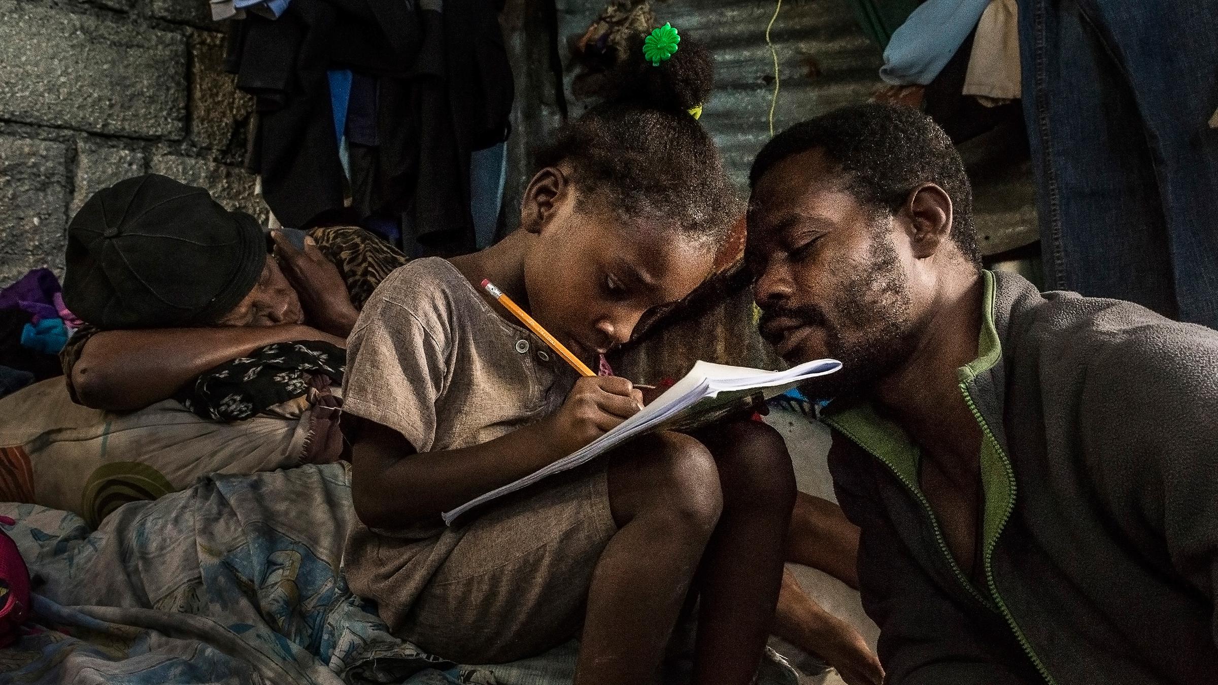 Vater auf Haiti hilft seiner 7-jährigen Tochter bei den Hausaufgaben 