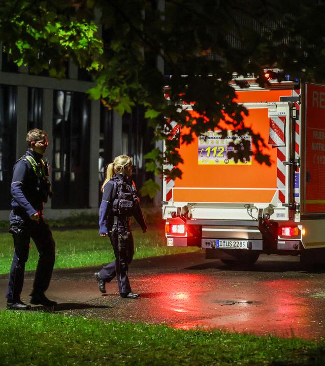 Polizisten laufen an einem ankommenden Rettungswagen vorbei, der eine deutsche Patientin in das Infektionszentrum der Uniklinik Düsseldorf bringt.