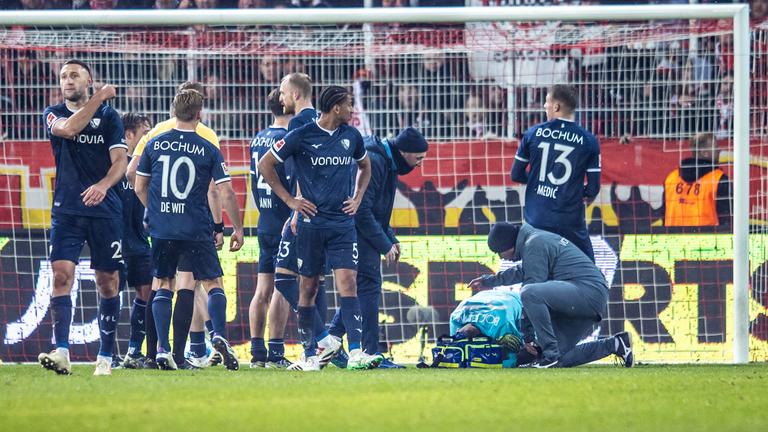 14.12.2024, Fußball-Bundesliga, 1. FC Union Berlin - VfL Bochum: VfL-Torwart Patrick Drewes kauert nach einem Feuerzeug-Treffer auf dem Boden, um ihn herum Spieler vom VfL Bochum