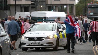 Menschen protestieren im Stadtzentrum von Sunderland, in der Mitte steht ein Polizeiauto.