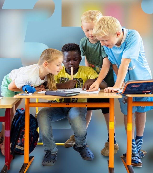Jerry sitzt am Tisch im Klassenraum und schreibt etwas. Alessia, Tom und Jan stehen daneben und schauen ihm zu.