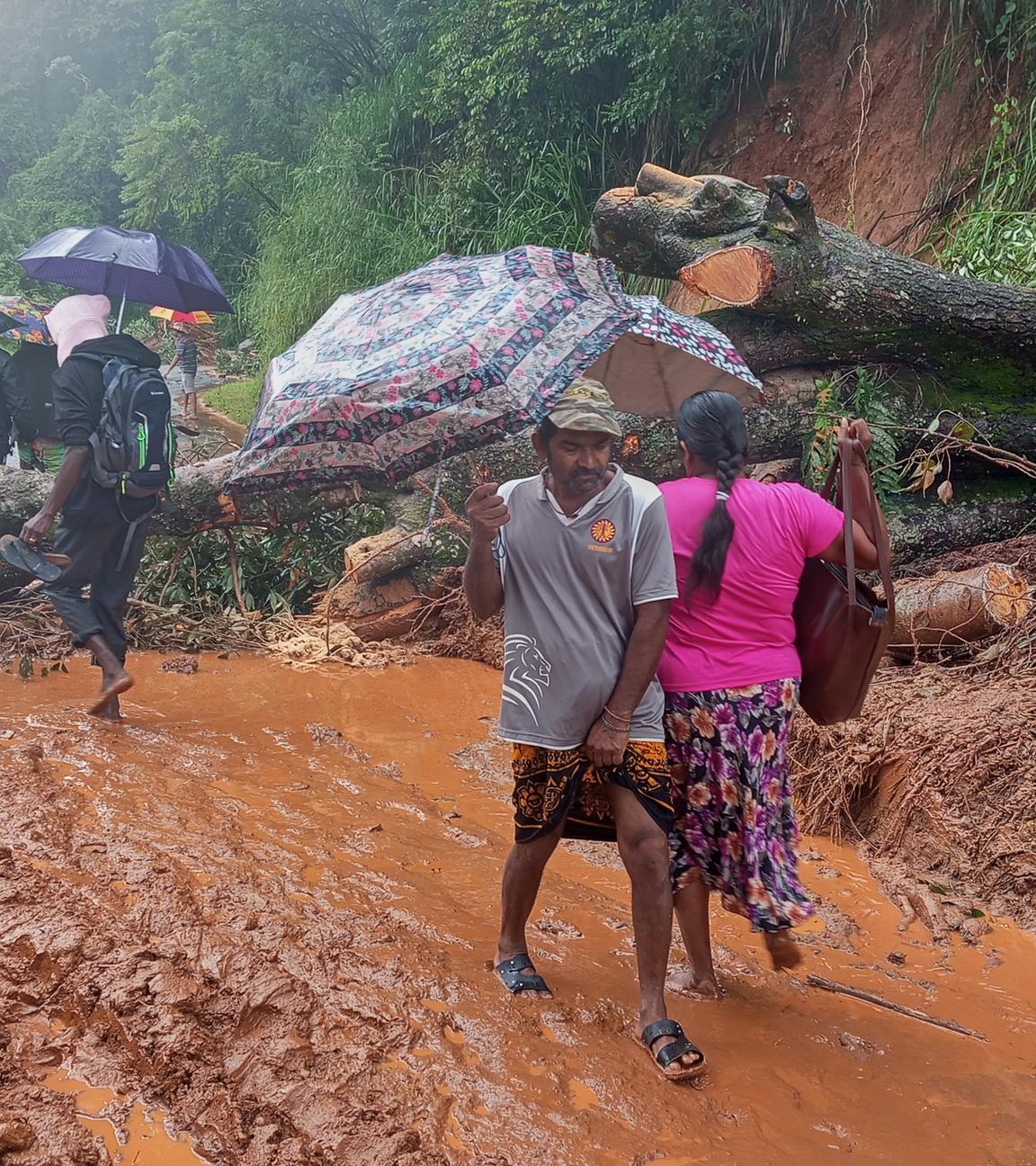 Überlebende eines Erdrutsches überqueren einen Straßenabschnitt, der durch Trümmer blockiert ist. 