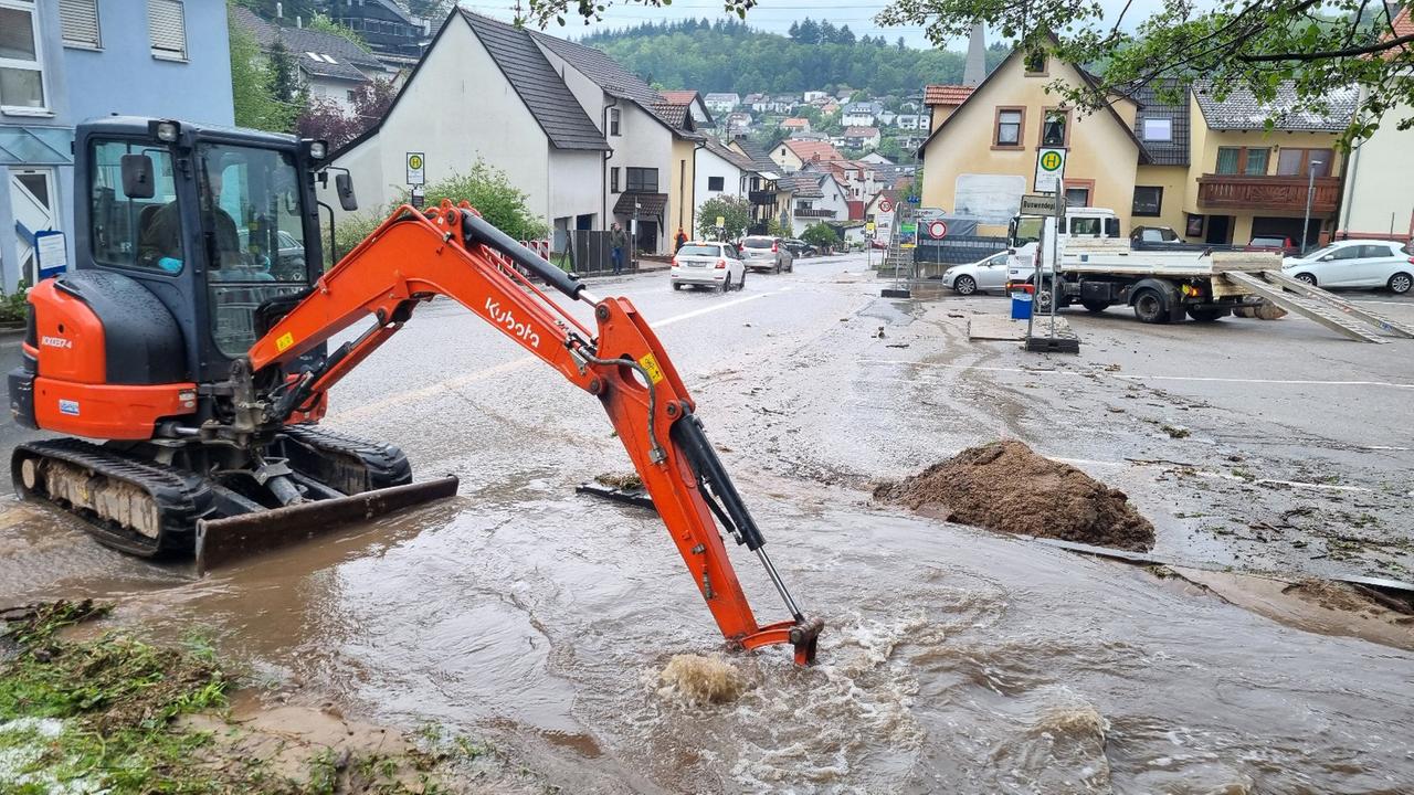 Baden-Württemberg, Schriesheim: Mit einem kleinen Bagger wird im Stadtteil Altenbach versucht den Bestbach frei zu schaufeln um das Wasser von der überfluteten Sraße abfließen zu lassen.