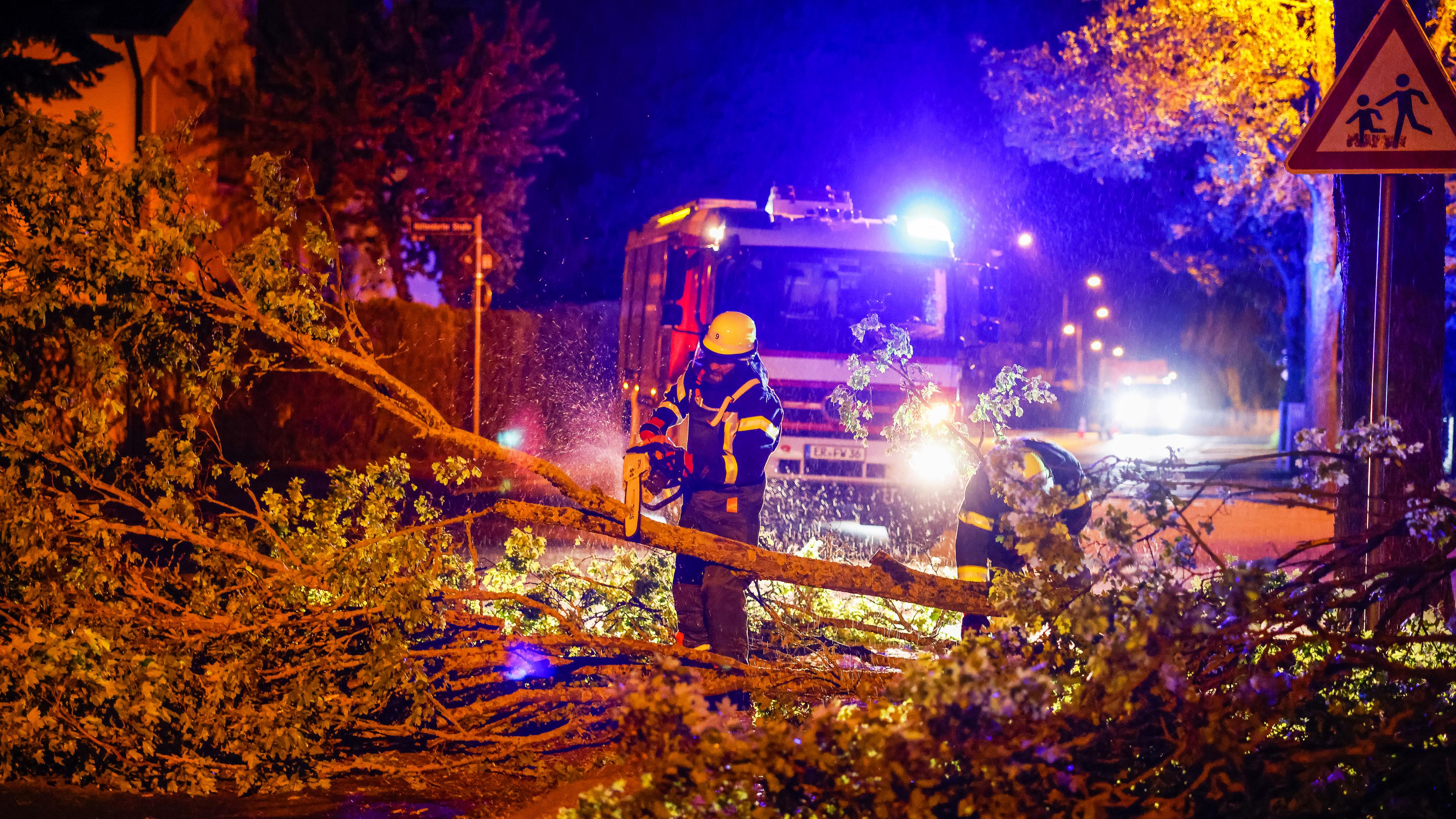 Einsatzkräfte der Feuerwehr zersägen mit einer Kettensäge einen umgestürzten Baum auf einer Straße im Regierungsbezirk Mittelfranken.