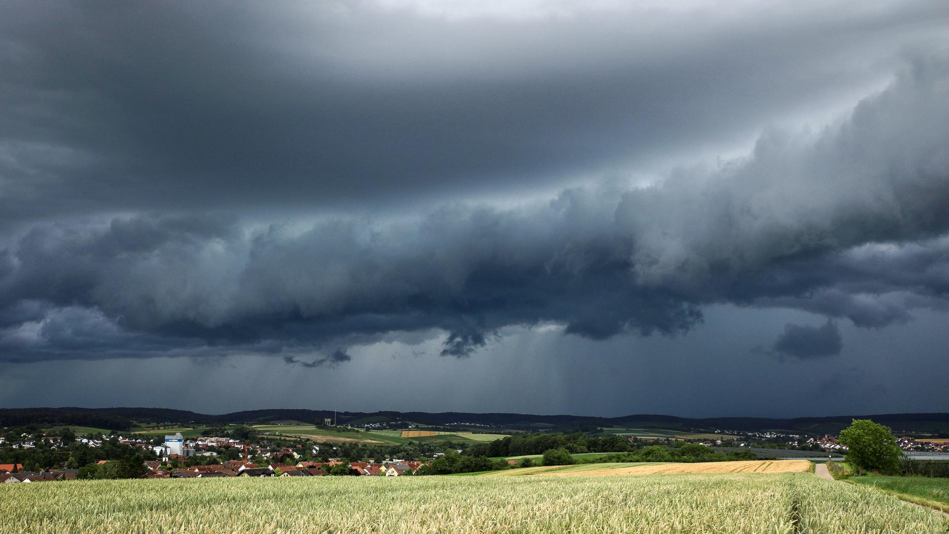 Baden-Württemberg, Heilbronn: Eine Gewitterzelle mit dunklen Wolken baut sich am Himmel und hinter Feldern nahe Heilbronn auf.