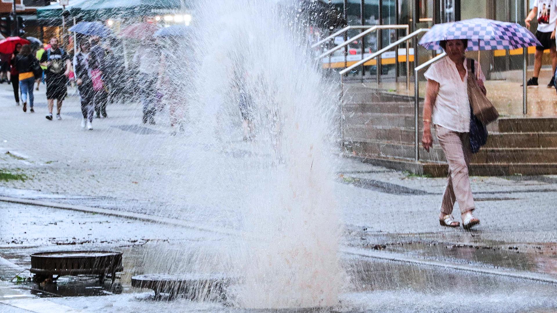 In einer Straße in Wuppertal spritzt nach heftigen Regenfällen das Wasser aus einem Gully, von dem der Deckel weggeflogen ist. Heftige Unwetter mit starken Regenfällen sind am 29.05.2018 über Nordrhein-Westfalen gezogen und haben Schäden vor allem in den Regionen Wuppertal und Aachen angerichtet