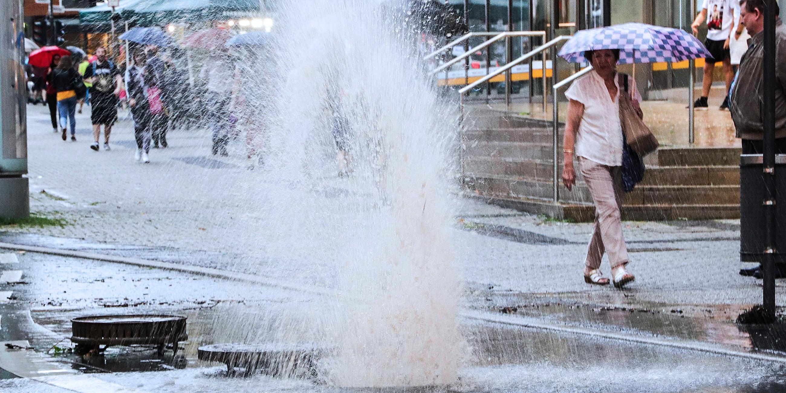 In einer Straße in Wuppertal spritzt nach heftigen Regenfällen das Wasser aus einem Gully, von dem der Deckel weggeflogen ist. Heftige Unwetter mit starken Regenfällen sind am 29.05.2018 über Nordrhein-Westfalen gezogen und haben Schäden vor allem in den Regionen Wuppertal und Aachen angerichtet