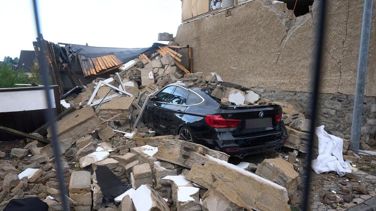 Gebäudeteile liegen nach einem Unwetter auf und um einem Auto. 