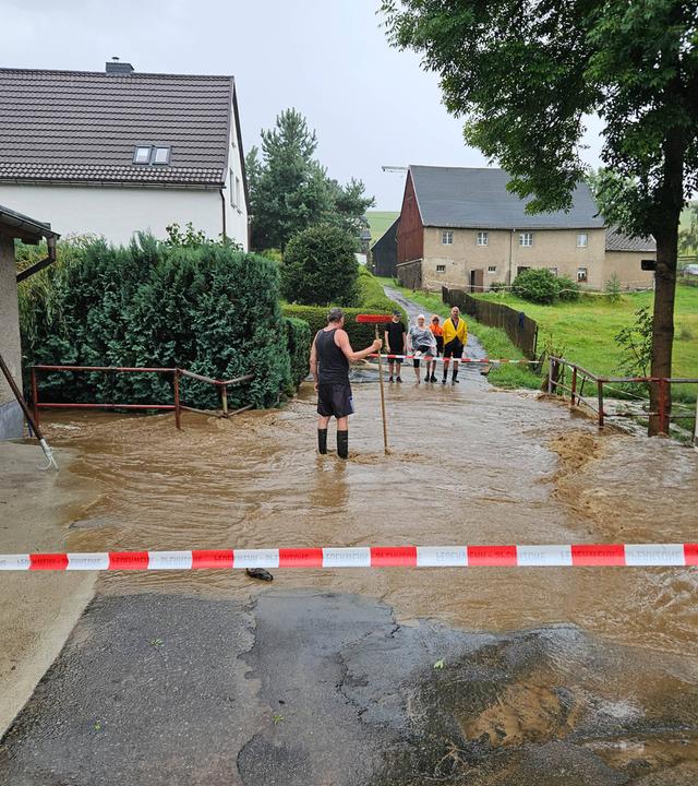 Teile Sachsen sind überflutet worden, sowie auf dem Bild erkennbar. Menschen stehen im Hochwasser.