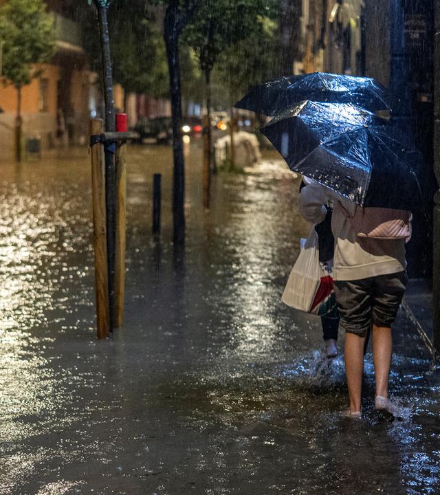 Menschen gehen über eien überflutete Straße in der spanischen Stadt L'Hospitalet de Llobregat. 